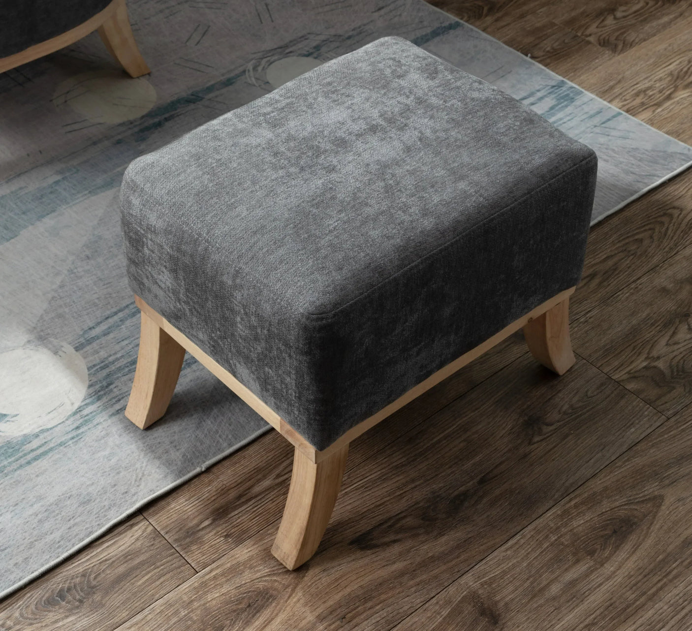 Grey fabric footstool with wooden legs on wood floor next to modern area rug