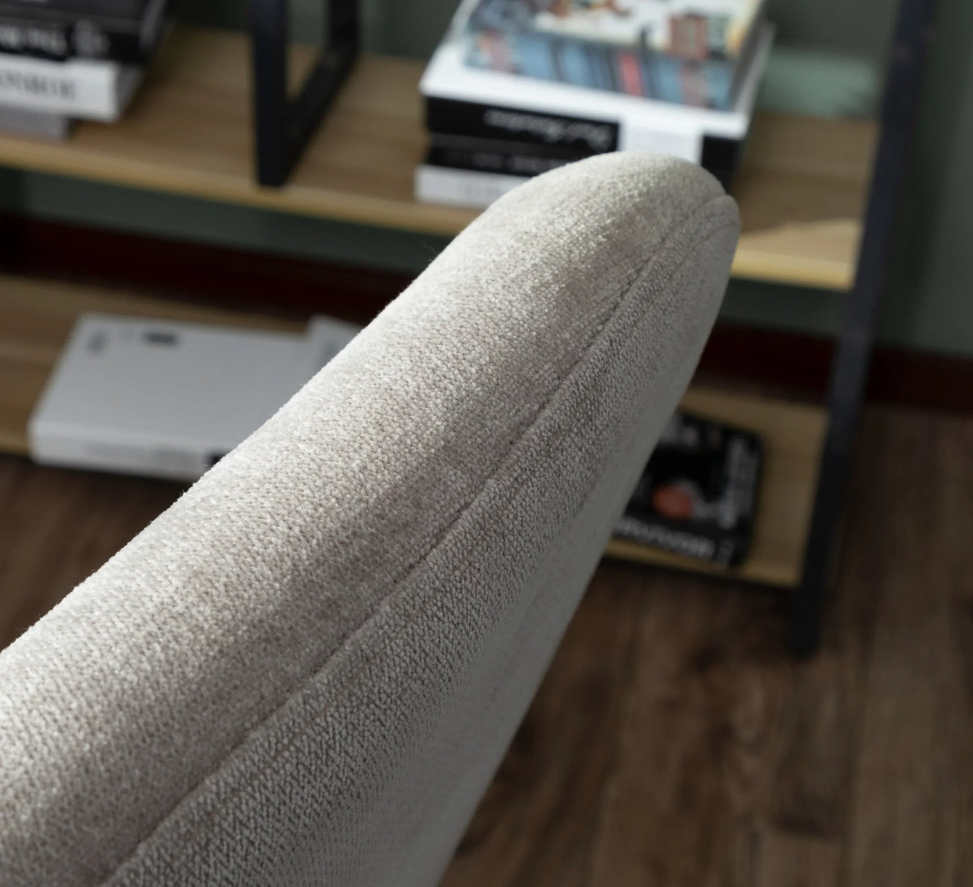 Close-up beige fabric sofa armrest with bookcase and wooden floor background