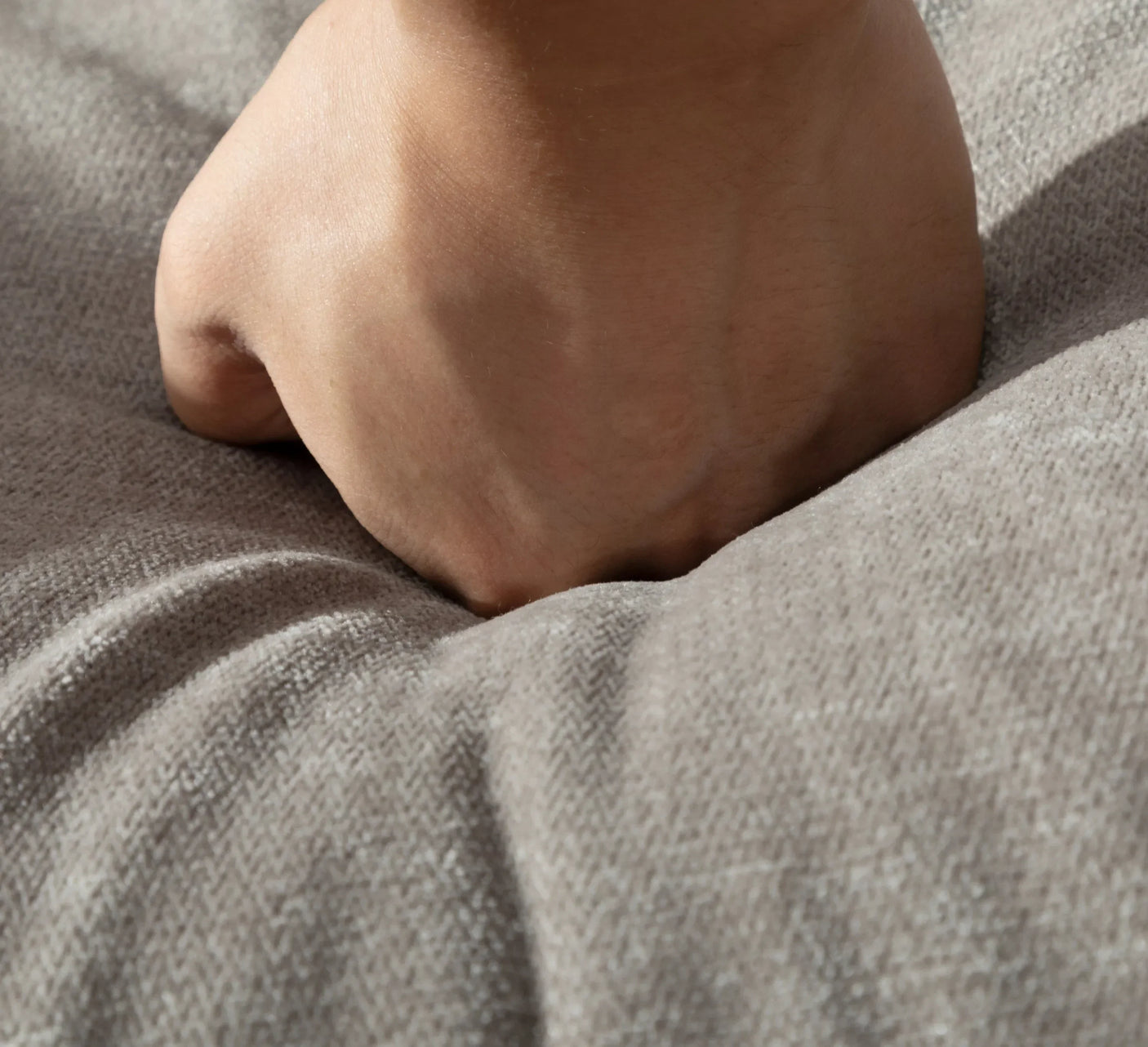 Hand pressing on soft grey sofa cushion showing fabric texture and comfort