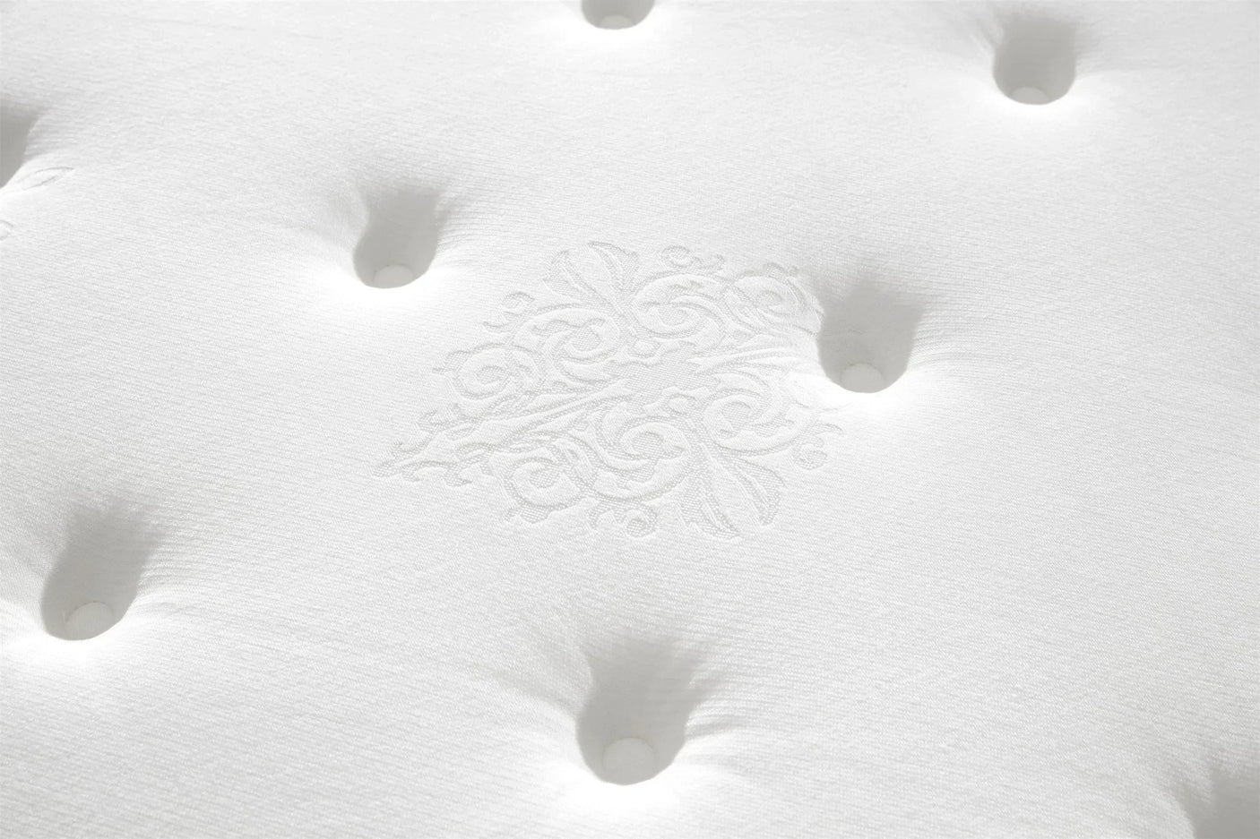 White mattress surface closeup with tufted detail and subtle floral pattern stitching