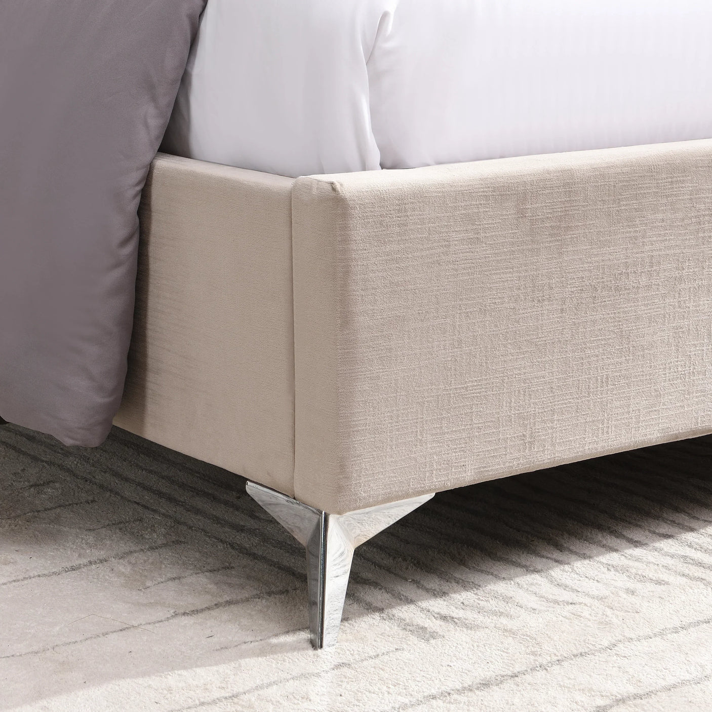 Beige upholstered bed frame with silver metal legs and textured fabric corner detail