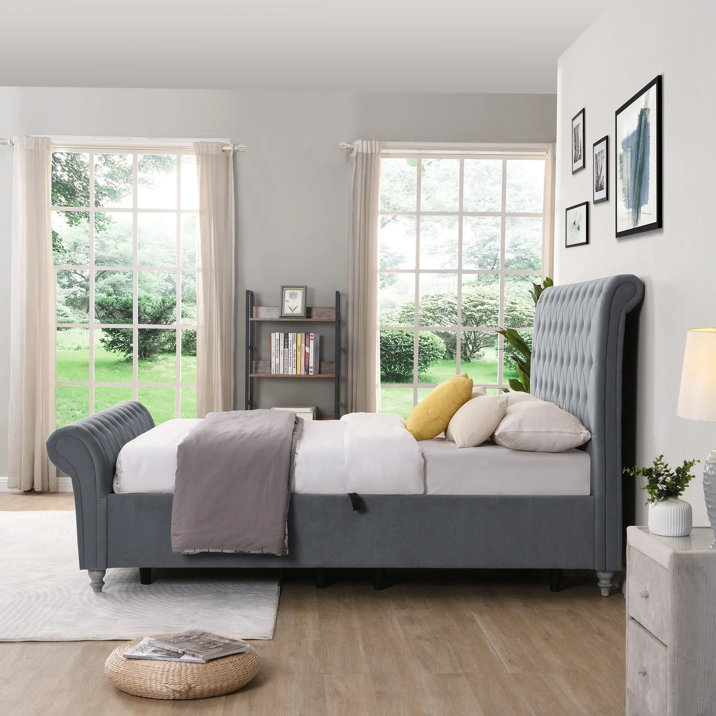 Grey upholstered bed with tufted headboard in bright bedroom with large windows and wood flooring