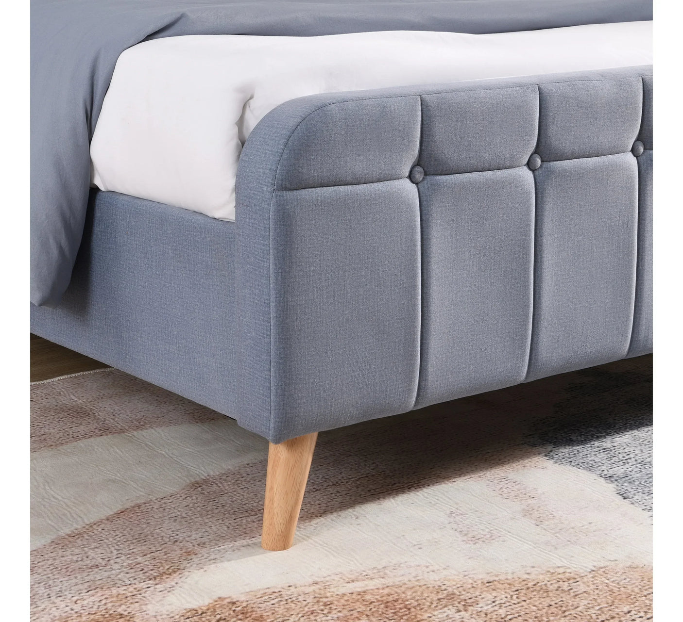 Light grey upholstered bed frame with rounded edge and wooden leg on patterned rug