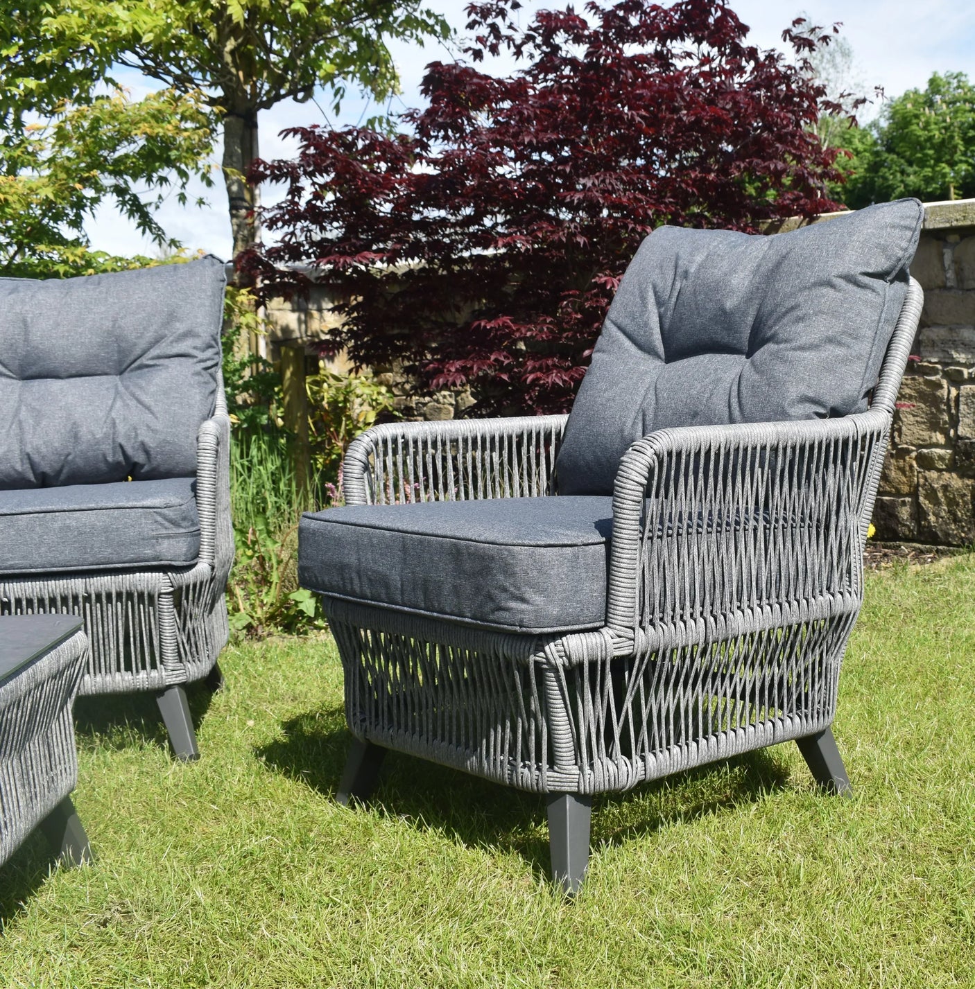 Grey rattan garden armchair with dark cushions on lawn
