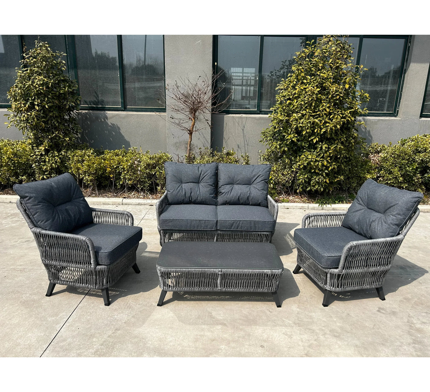 Grey rattan outdoor furniture set with cushioned sofa, two armchairs and coffee table