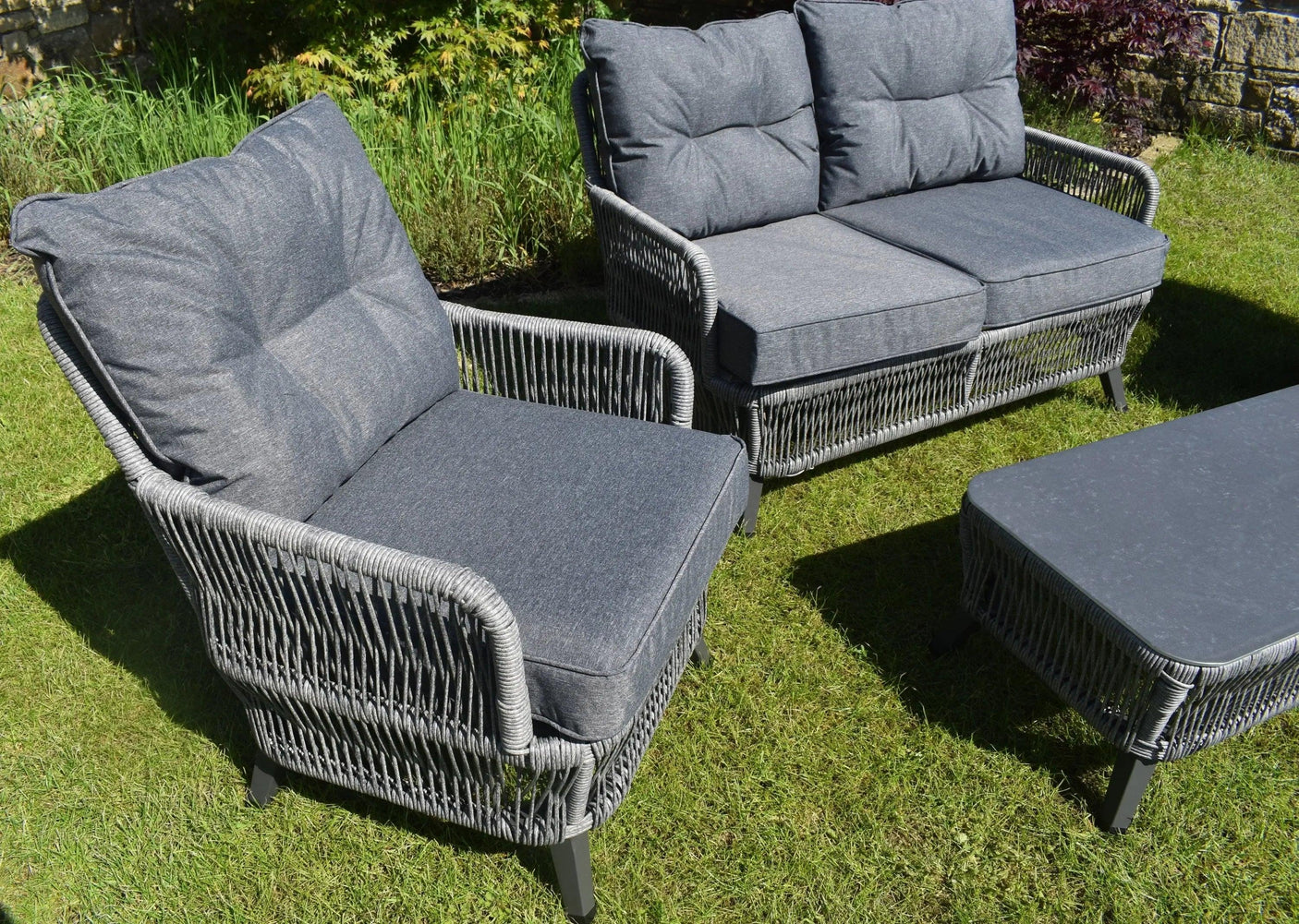Grey rattan garden furniture set with cushioned armchair, sofa and coffee table on lawn