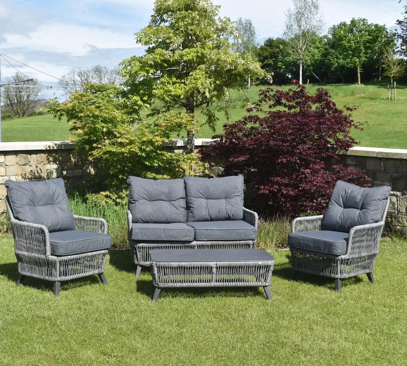 Grey rattan outdoor garden furniture set with cushions, coffee table, chairs and sofa on lawn