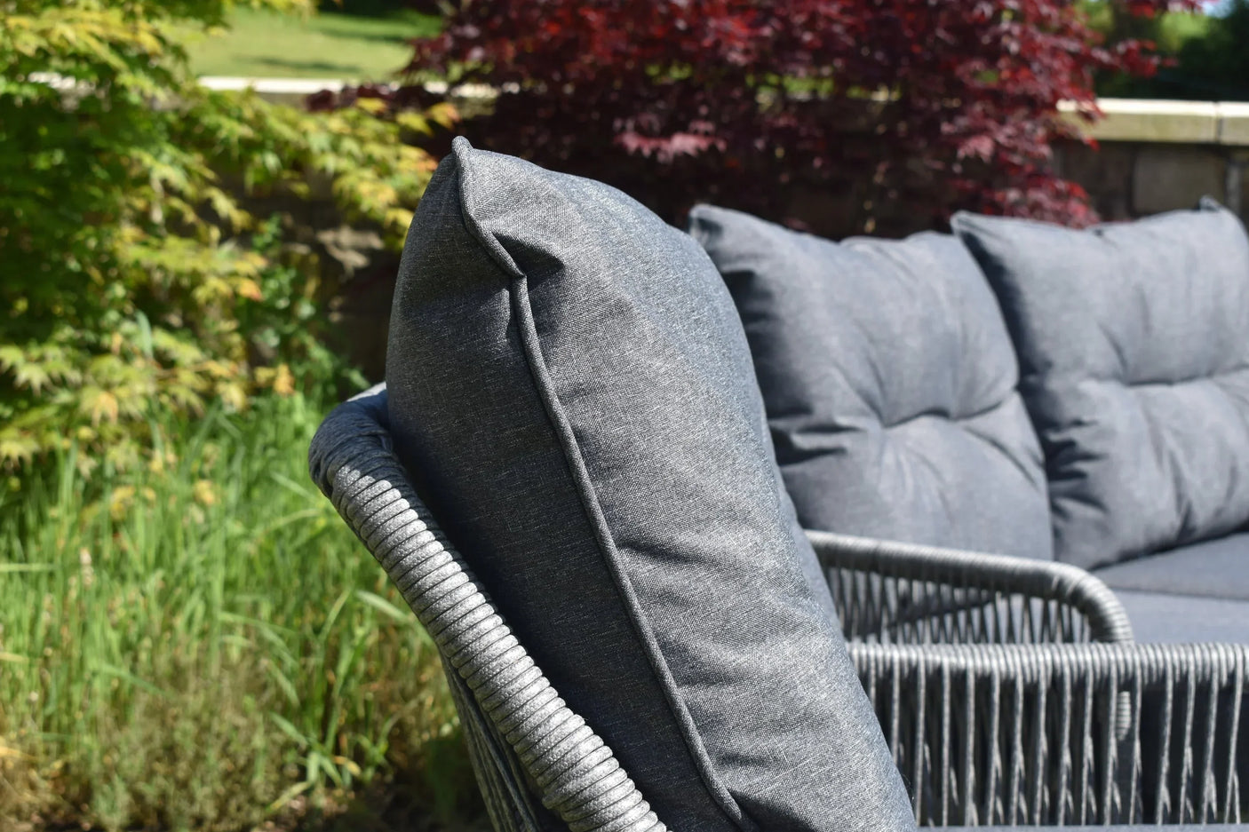 Close-up of grey outdoor sofa with rope frame and plush cushions in garden