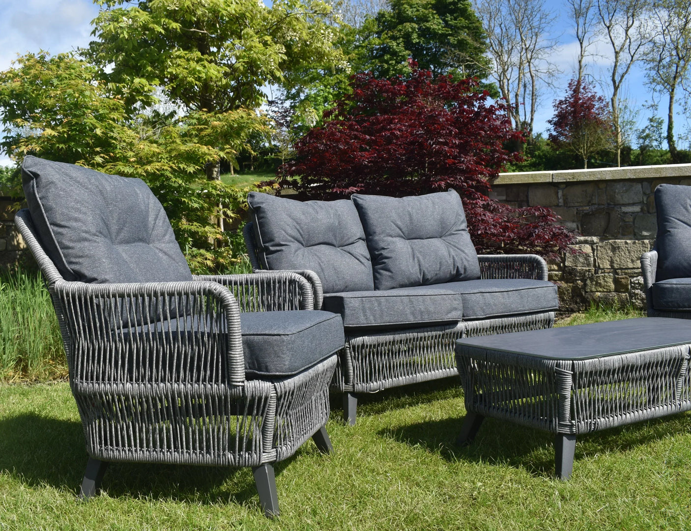 Grey rattan outdoor sofa set with cushioned seating and coffee table on lawn