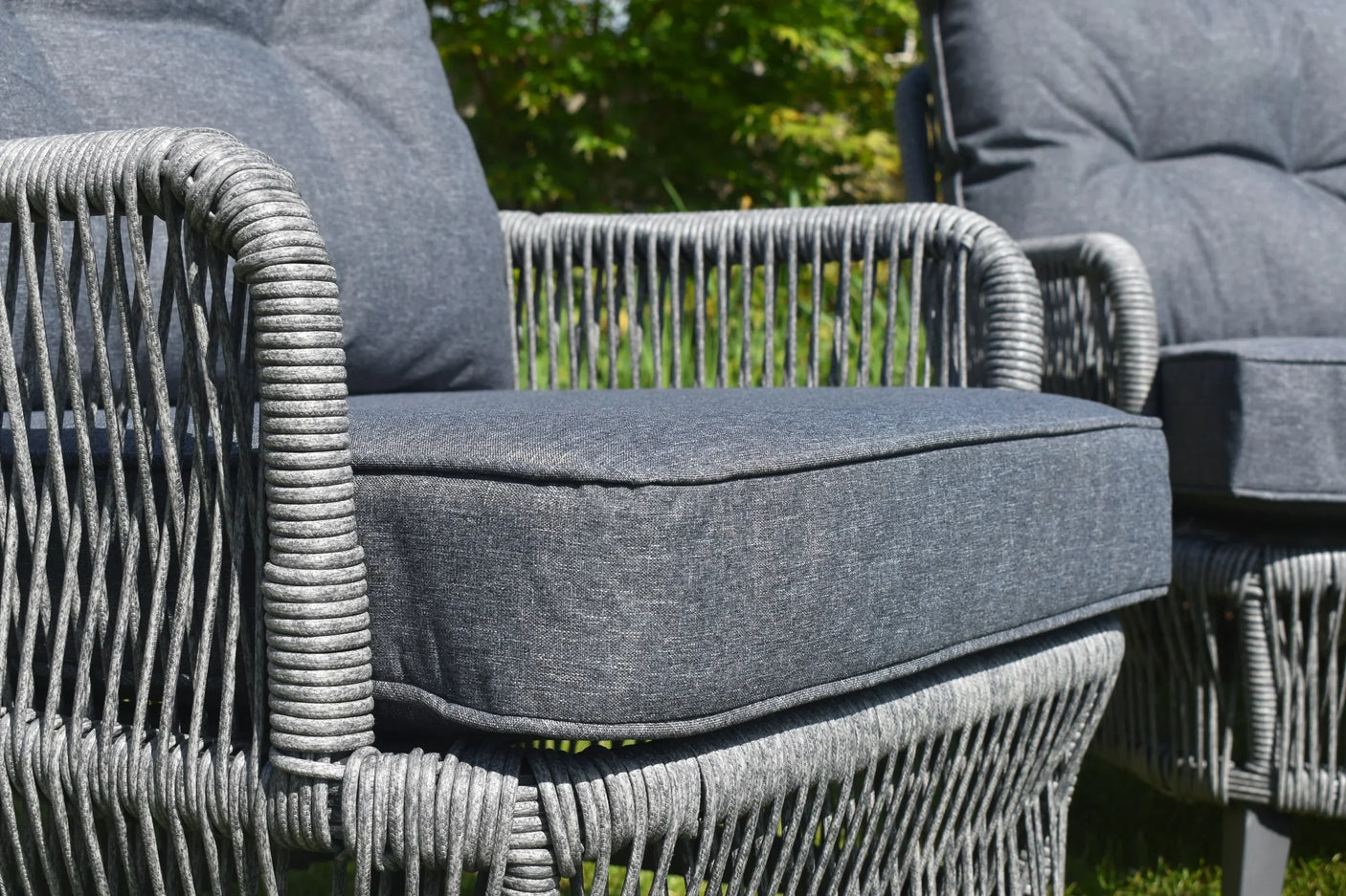 Grey rattan outdoor chair with deep cushions and woven armrest detail