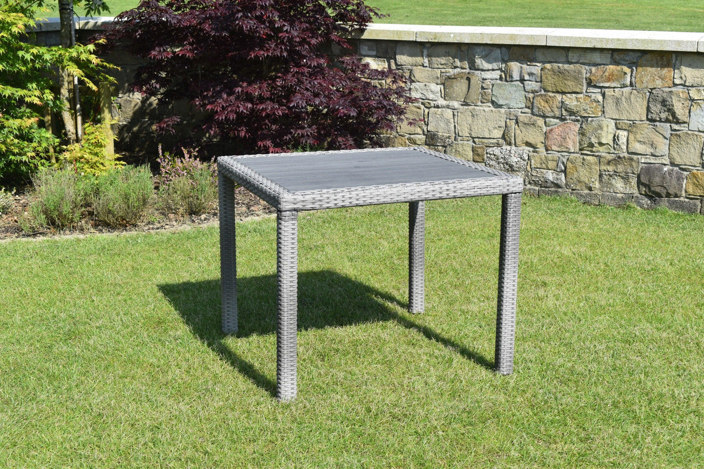 Grey rattan outdoor dining table with square top on grass garden lawn