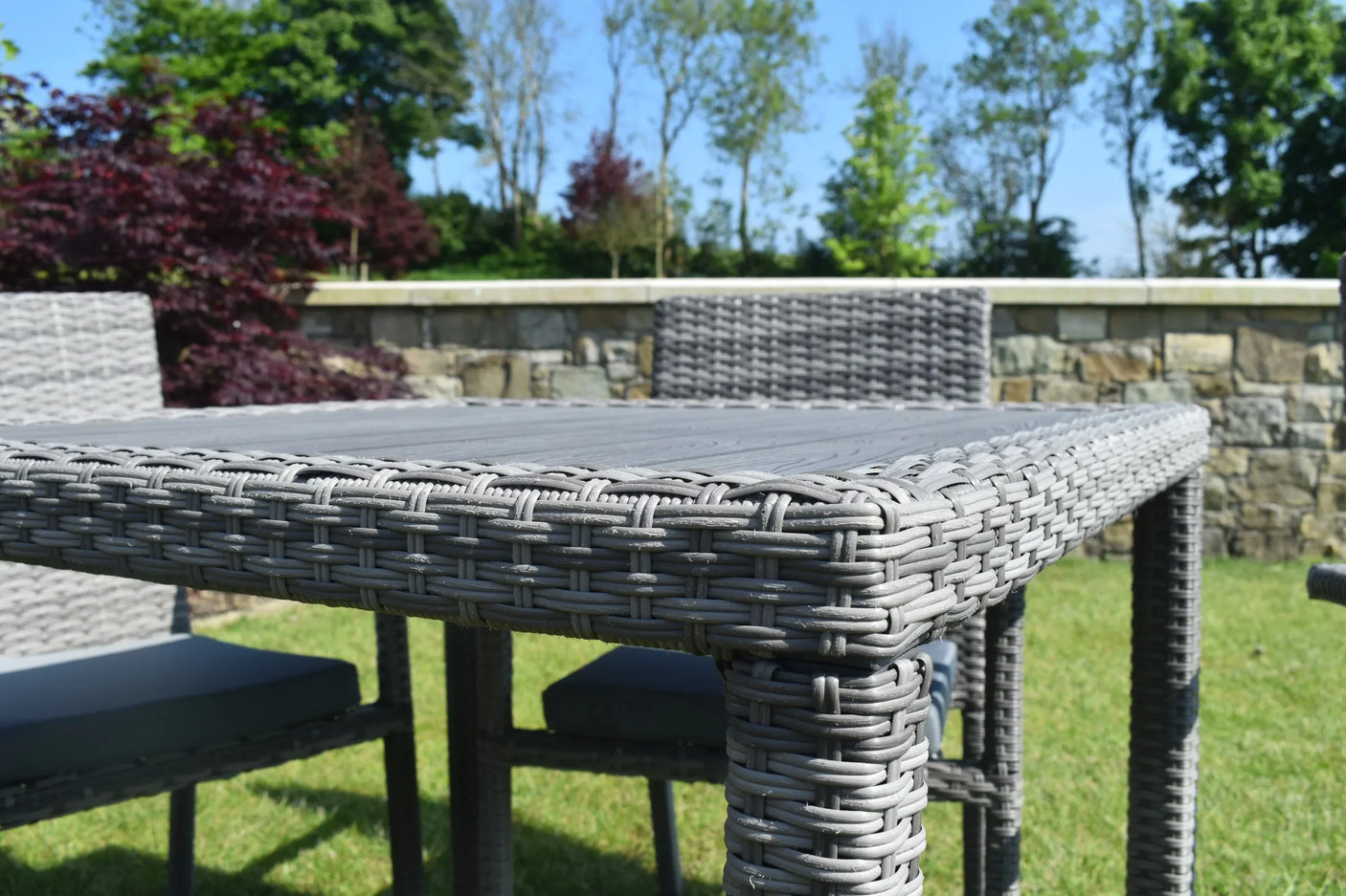 Grey rattan outdoor dining table and chairs on grass with stone wall