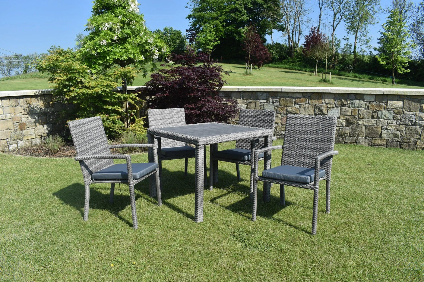 Grey rattan garden dining set with four cushioned chairs and square table on lawn