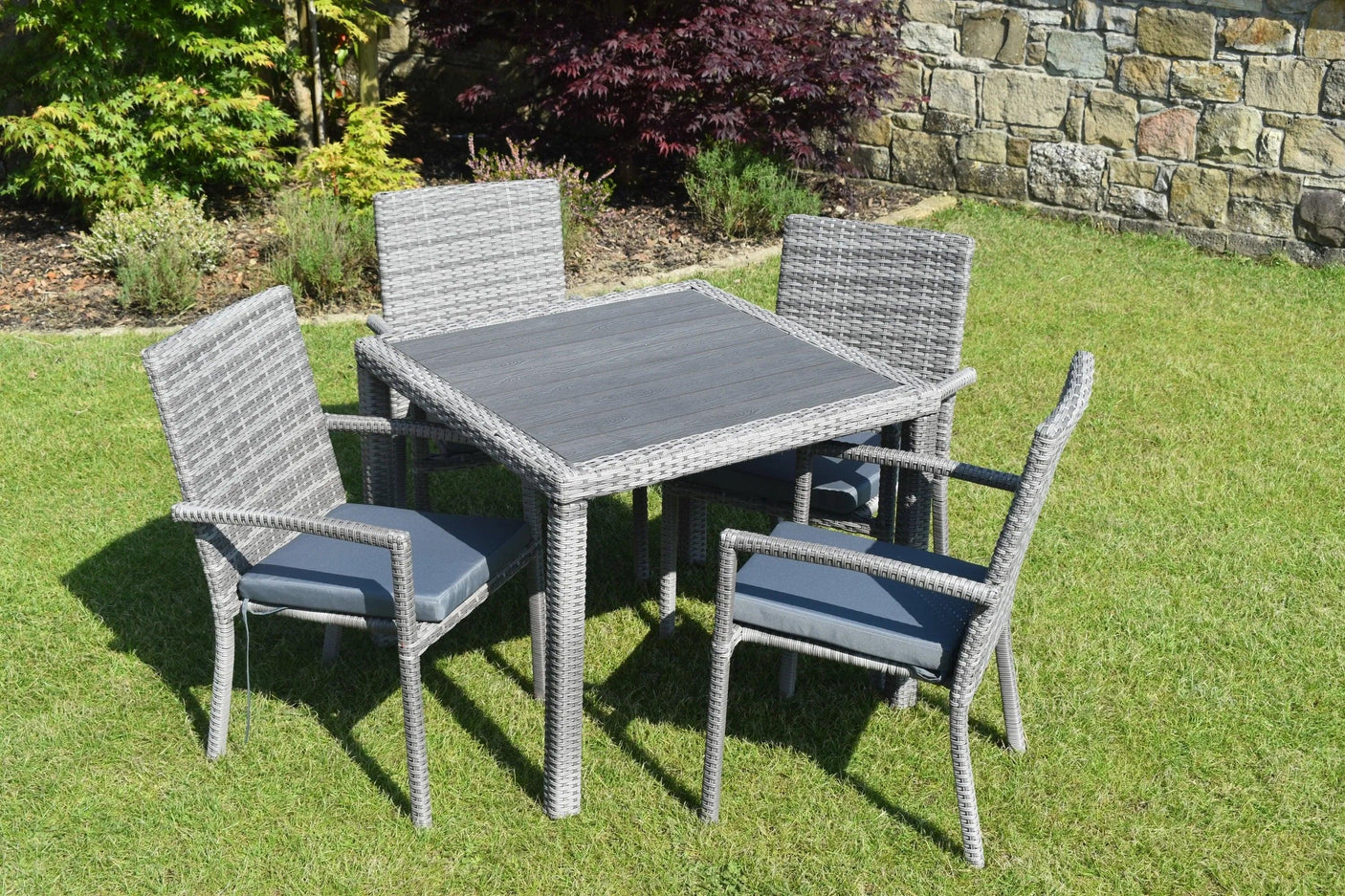 Grey rattan garden dining set with square table and four cushioned chairs on lawn