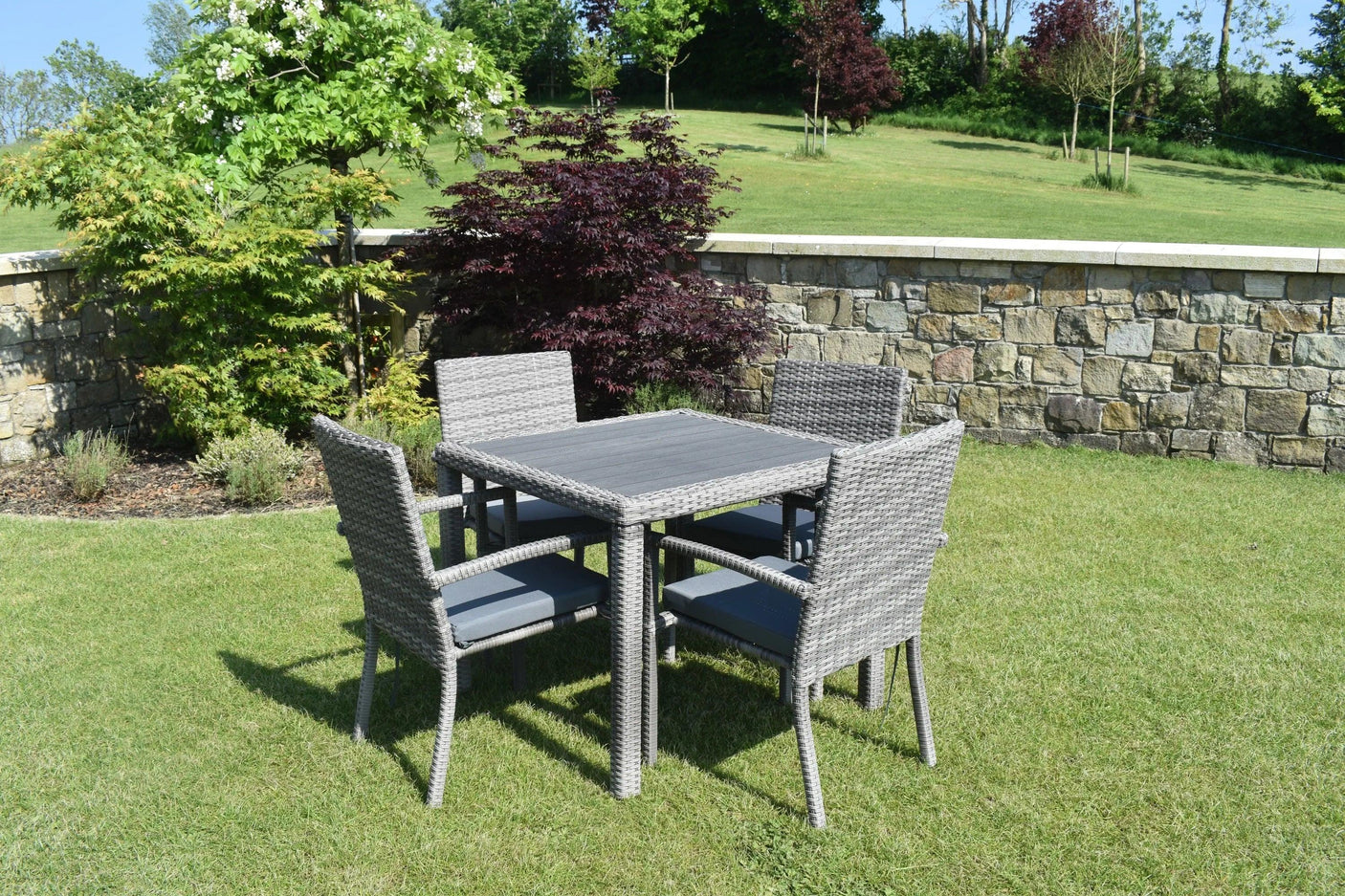 Grey rattan garden dining set with square table and four cushioned chairs on lawn