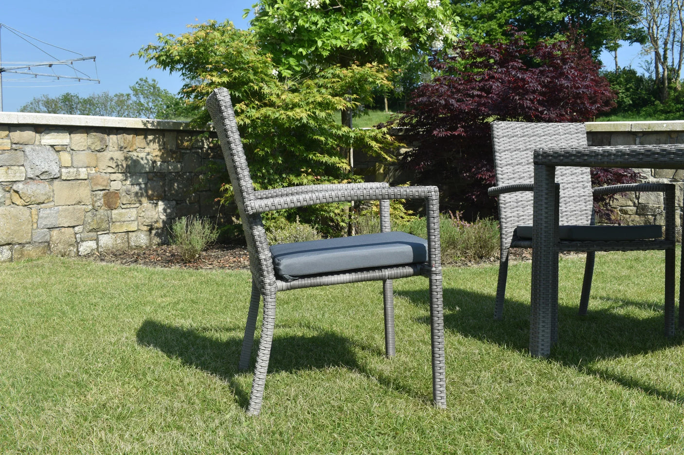 Grey rattan garden chair with armrests and dark cushion on grass patio set outdoors
