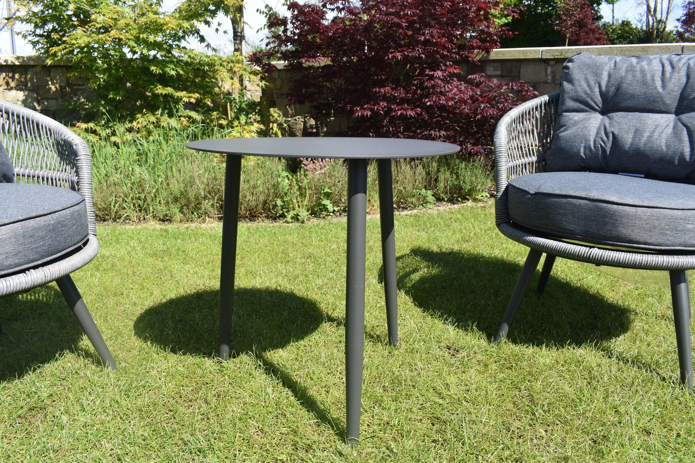 Outdoor garden furniture set with round grey table and cushioned rattan armchairs on grass