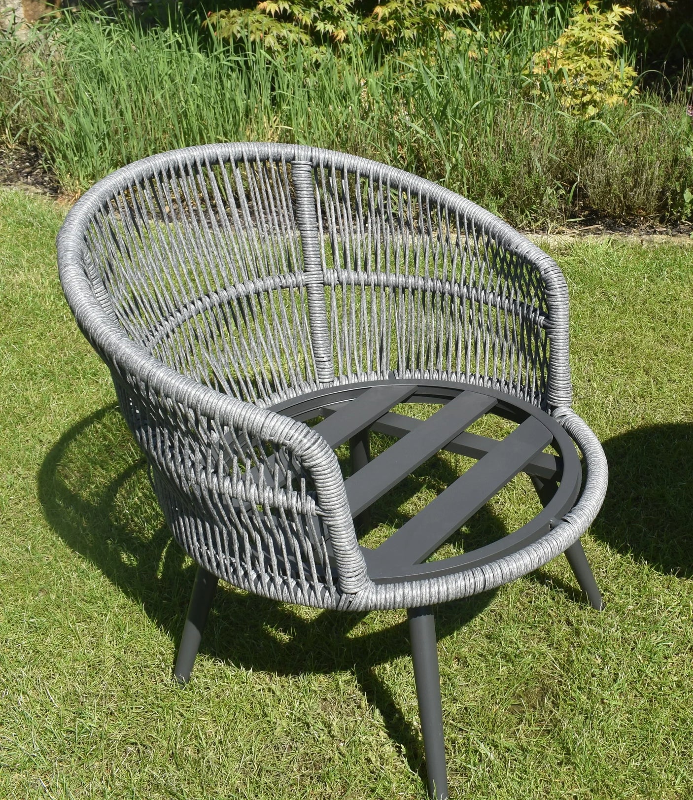 Grey rattan garden chair with round frame and wide backrest on grass lawn