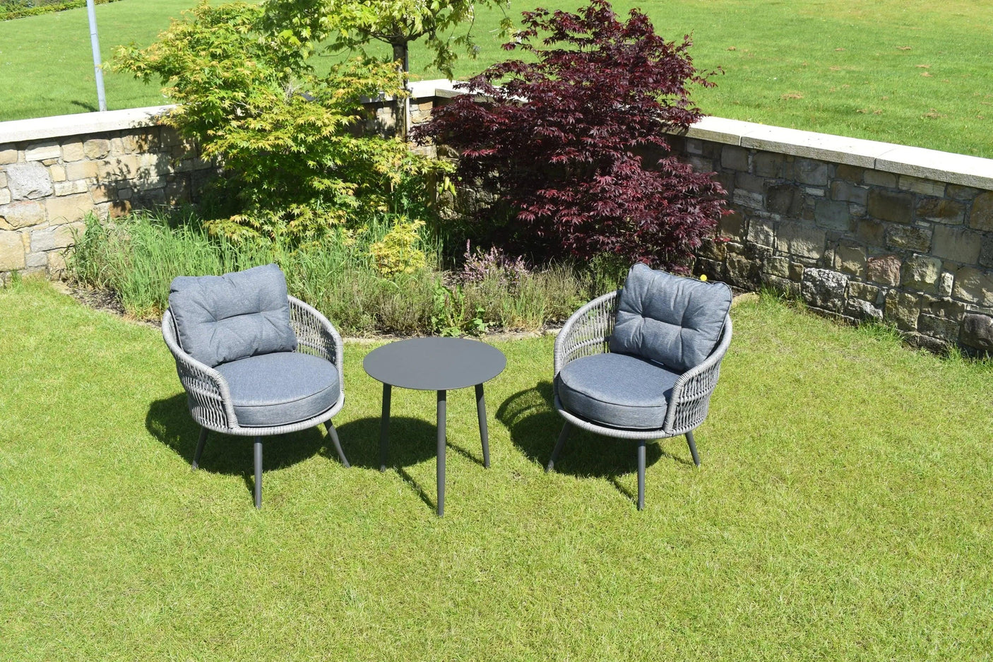 Grey rattan garden furniture set with two cushioned chairs and round table on lawn