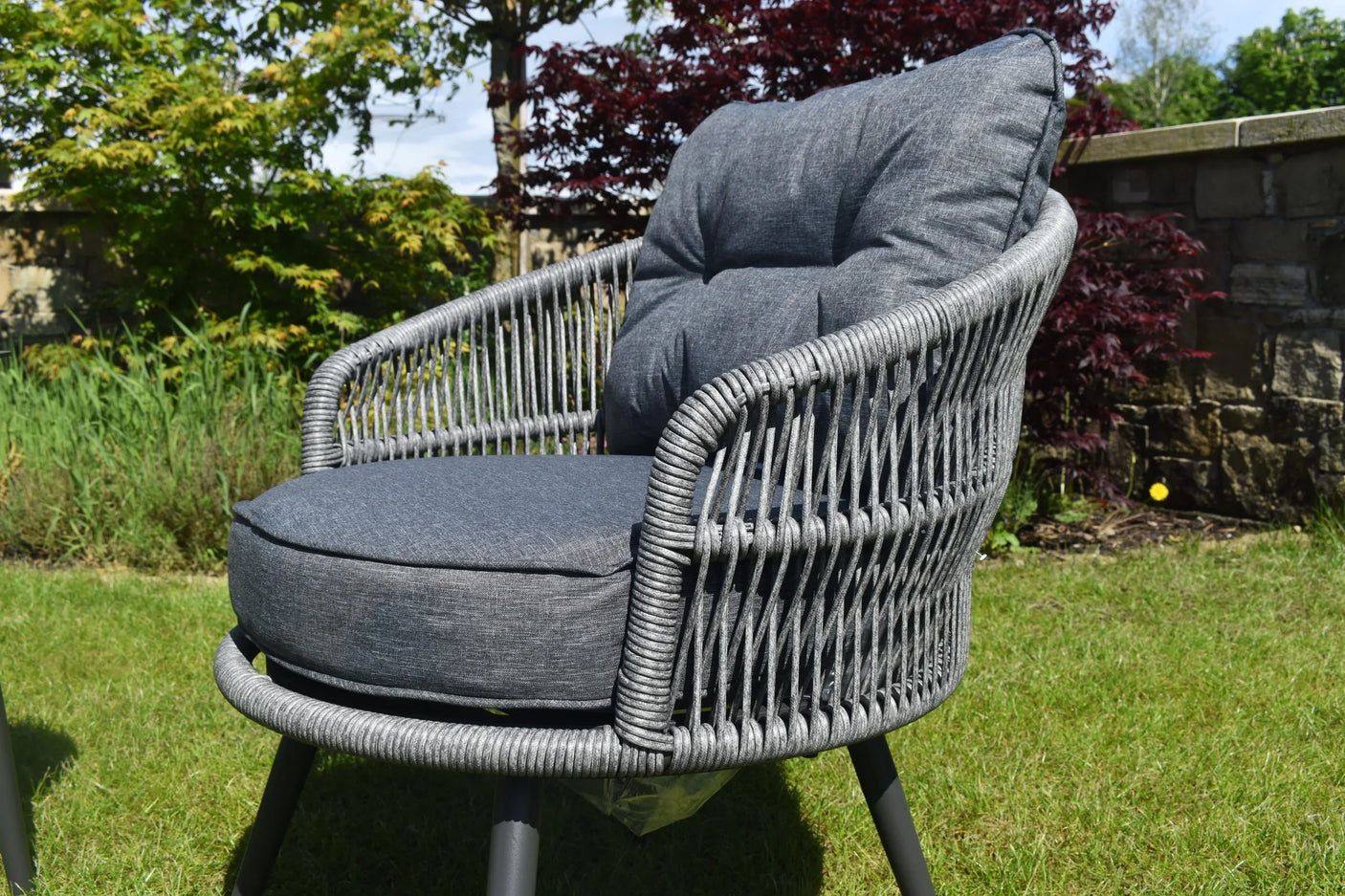 Grey rattan garden chair with padded cushions on lawn outdoor setting