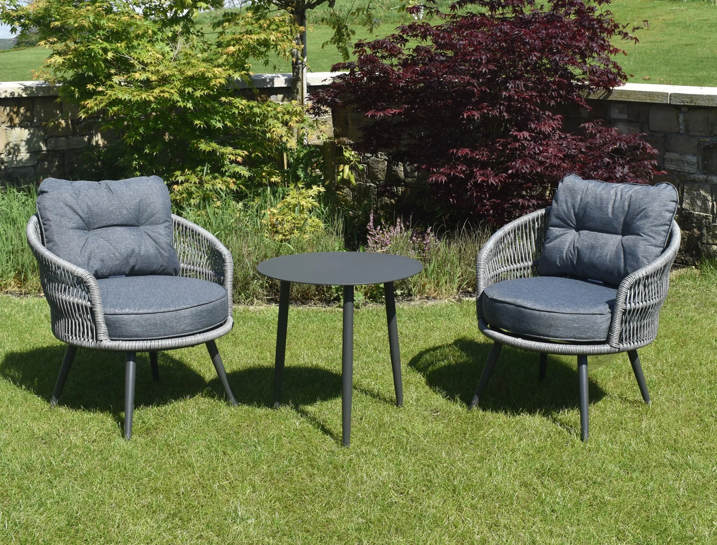 Rattan garden furniture set with two grey cushioned chairs and round black table on lawn