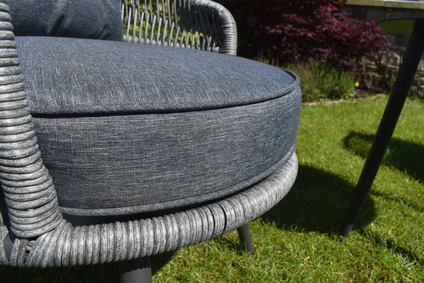 Close up of grey rattan garden dining chair with woven frame and padded seat cushion outdoors