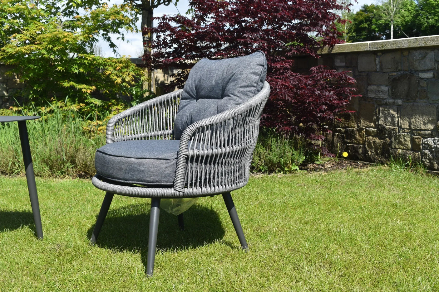 Grey rattan garden armchair with dark cushions on lawn beside outdoor table