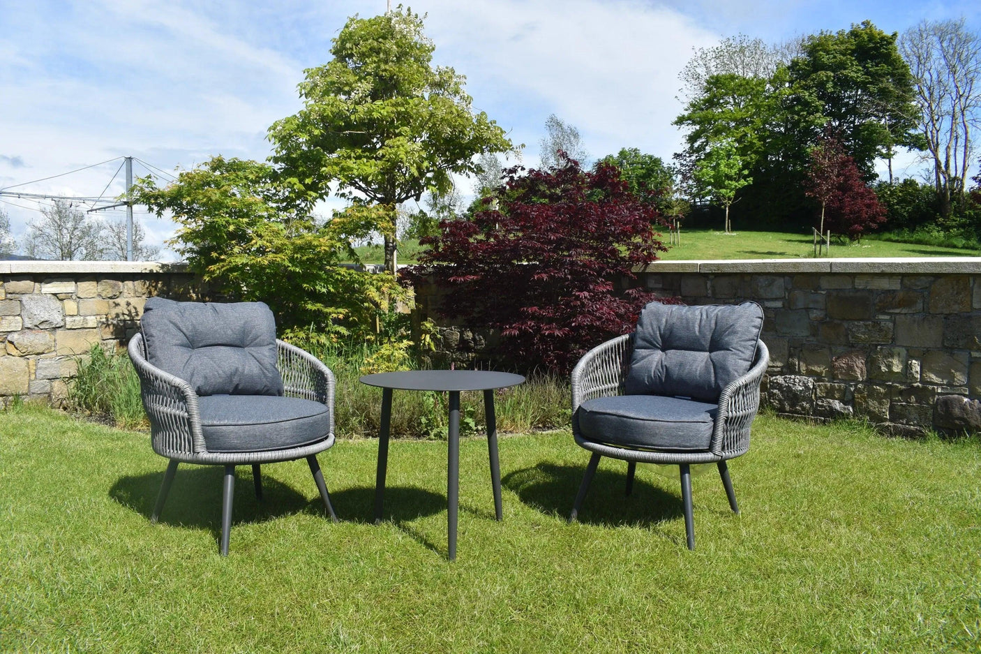 Grey rattan garden bistro set with two cushioned chairs and round table on grass
