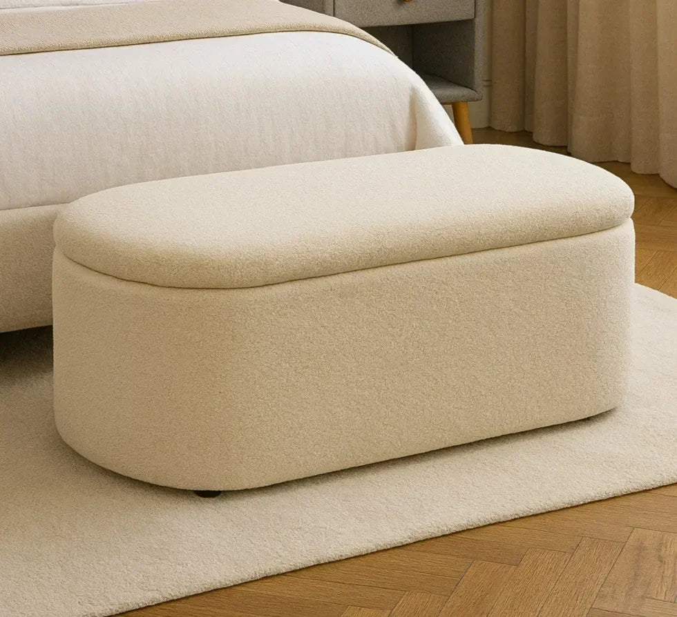 Beige fabric ottoman bench with storage at end of bed on cream rug and wooden floor