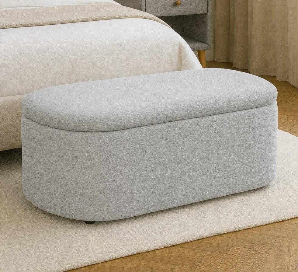Light grey ottoman bench with fabric upholstery at the end of a bed in a modern bedroom