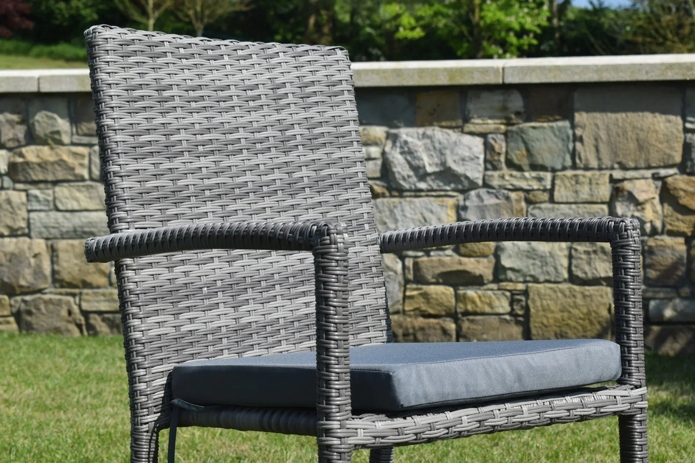 Grey rattan garden chair with armrests and seat cushion on lawn