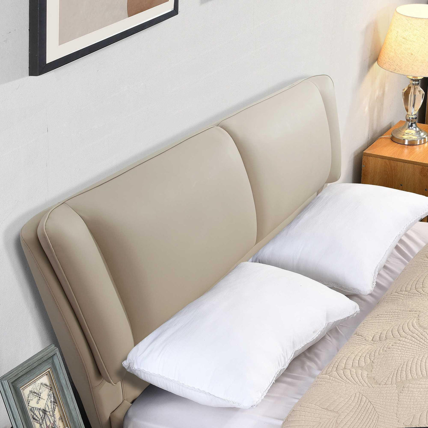 Beige upholstered bed headboard with two white pillows and bedside table with lamp