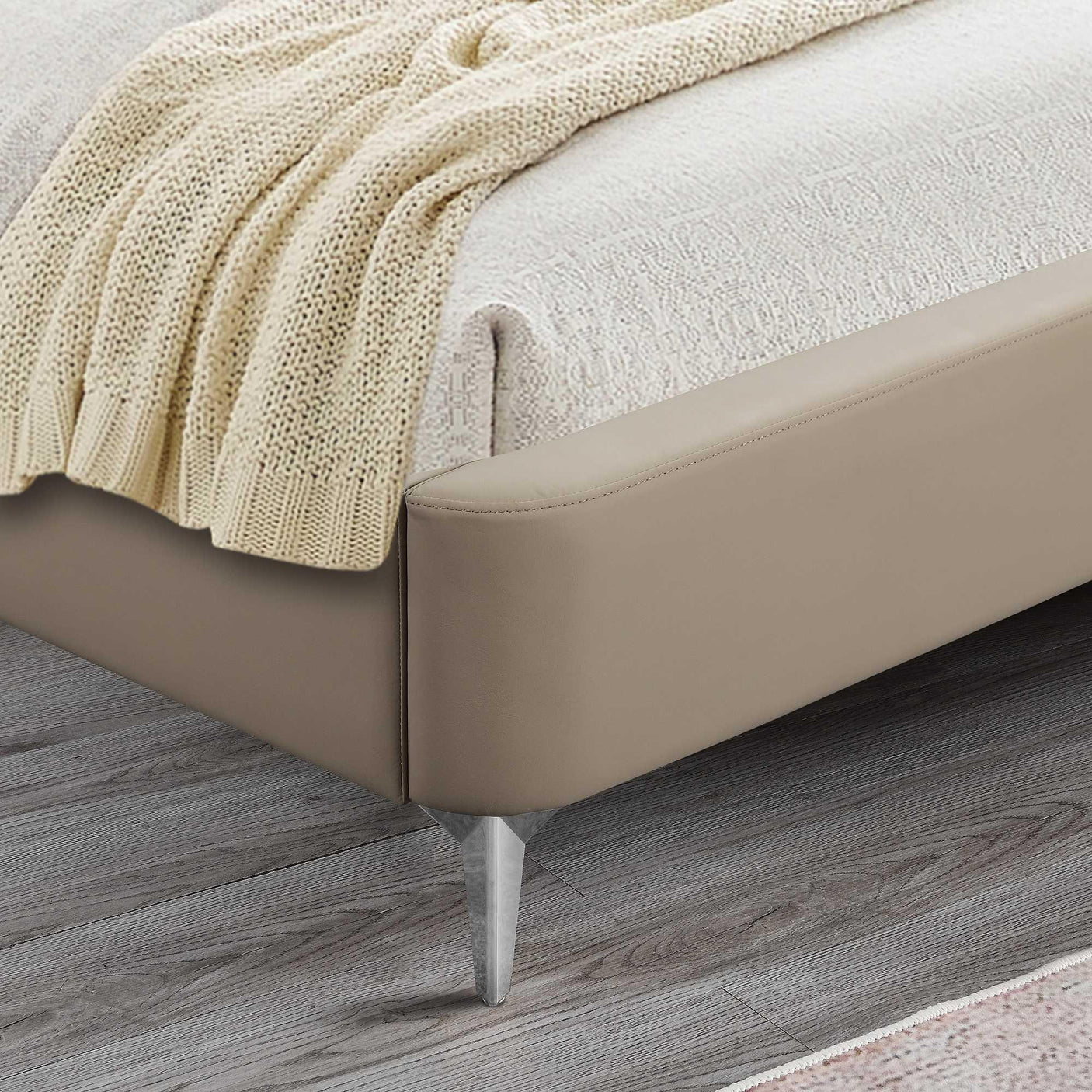 Beige upholstered bed frame corner with chrome leg and cream knit throw on bedding