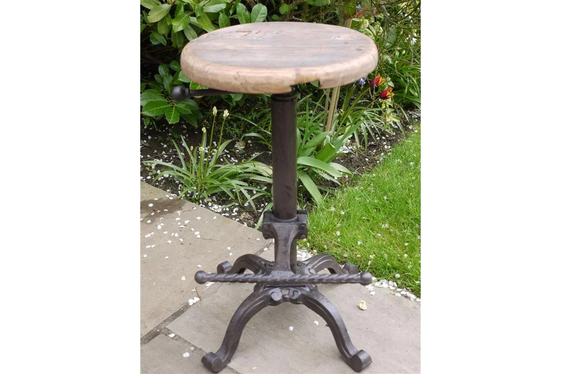 Round wooden bar stool with cast iron base on patio beside garden plants