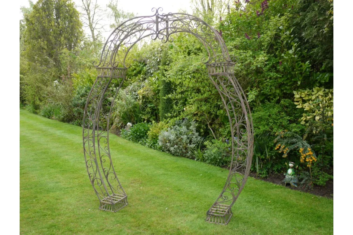 Decorative metal garden arch with scrollwork design on lawn near green shrubbery