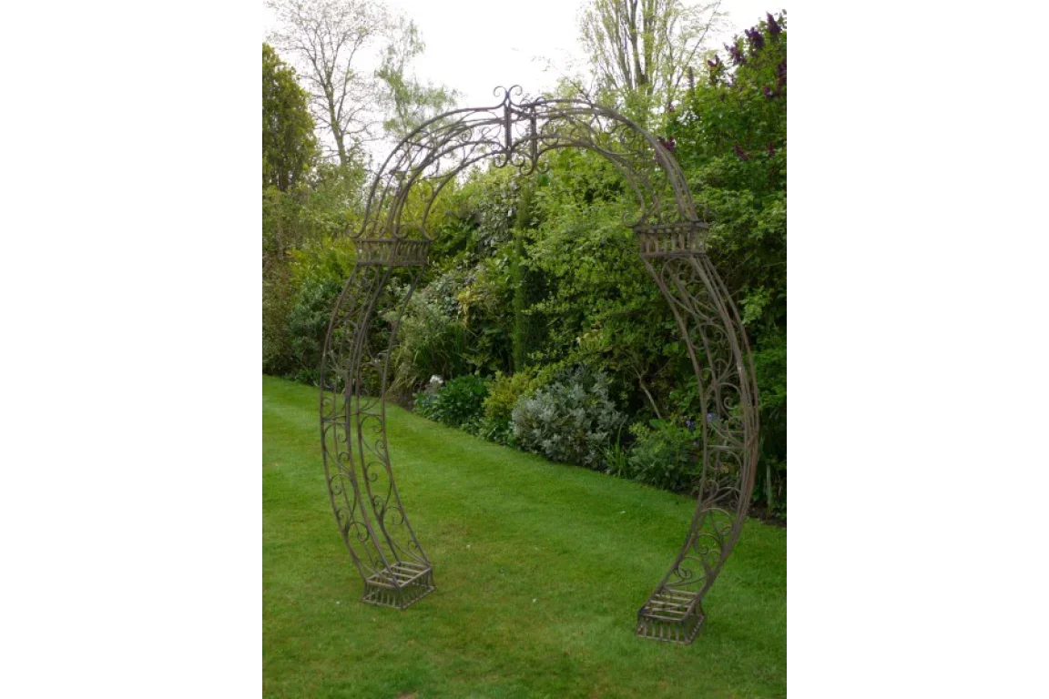 Decorative metal garden arch with ornate scrollwork placed on a lawn with green foliage