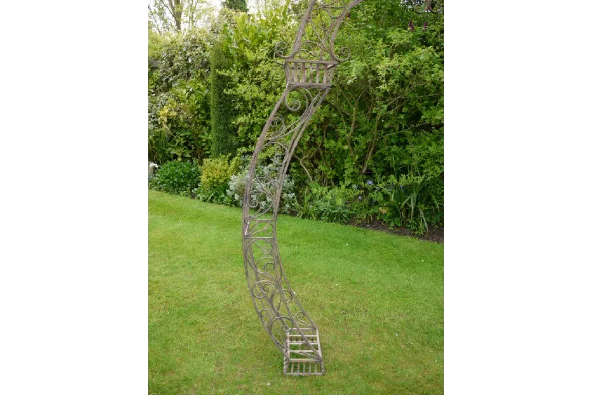 Curved metal garden arch with scrollwork design placed on green lawn near hedges