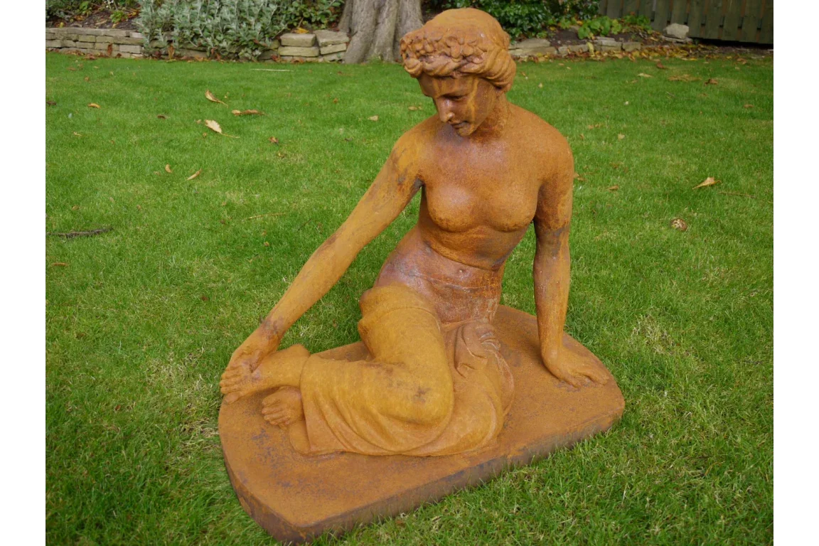 Seated cast iron female garden statue with rust finish on lawn