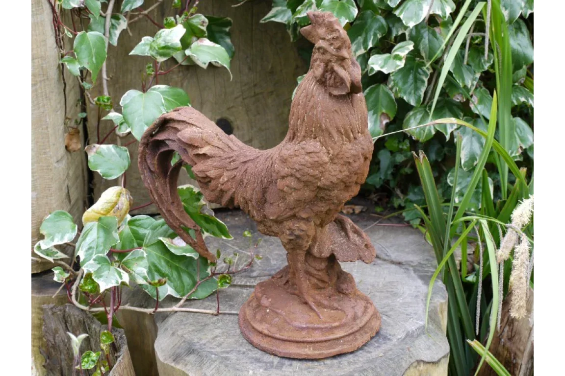Rust effect rooster garden ornament on wooden stump with green foliage background