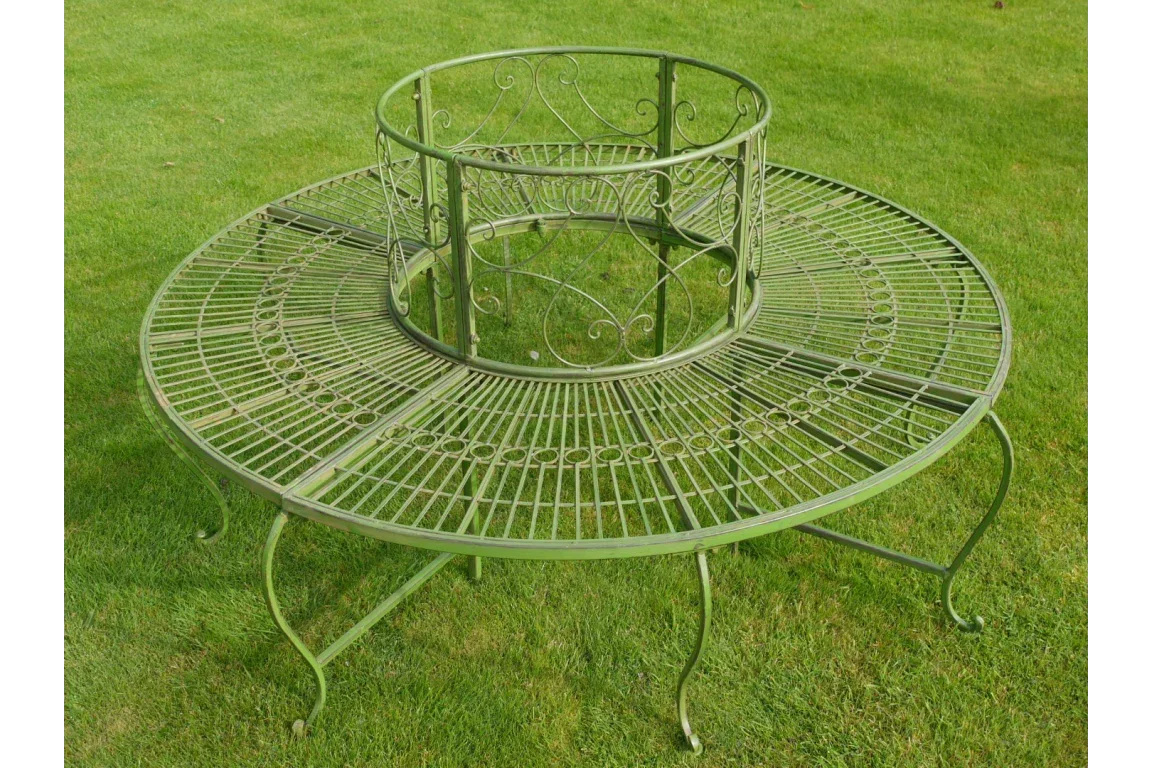 Green metal tree bench with decorative scroll design on garden lawn