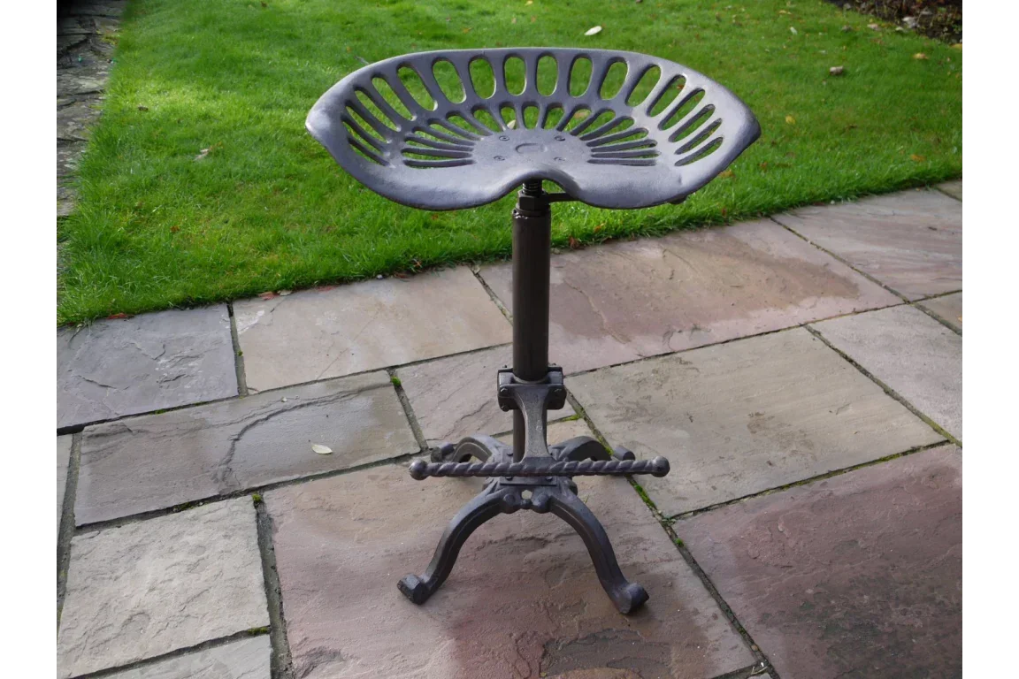 Industrial metal tractor seat bar stool with footrest on stone patio