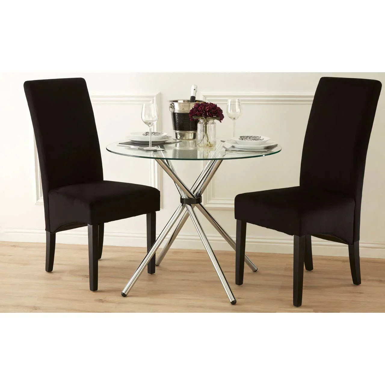 Glass dining table with chrome legs and two black upholstered dining chairs