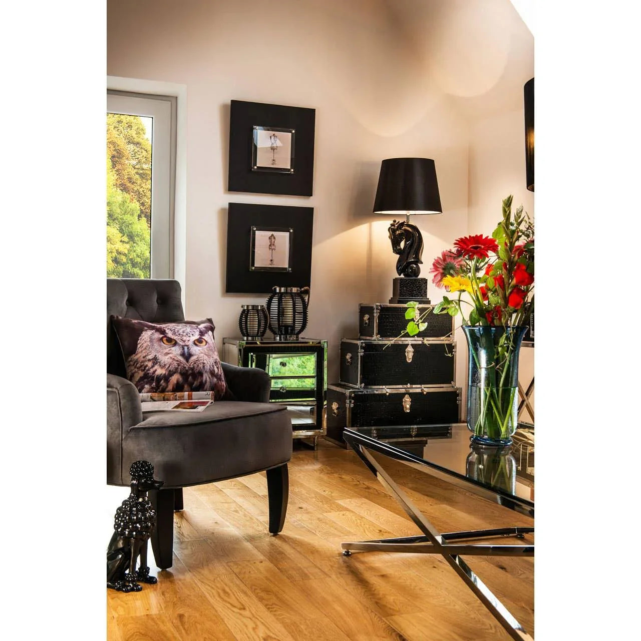 Living room with grey armchair, owl cushion, black side table, and stacked storage trunks