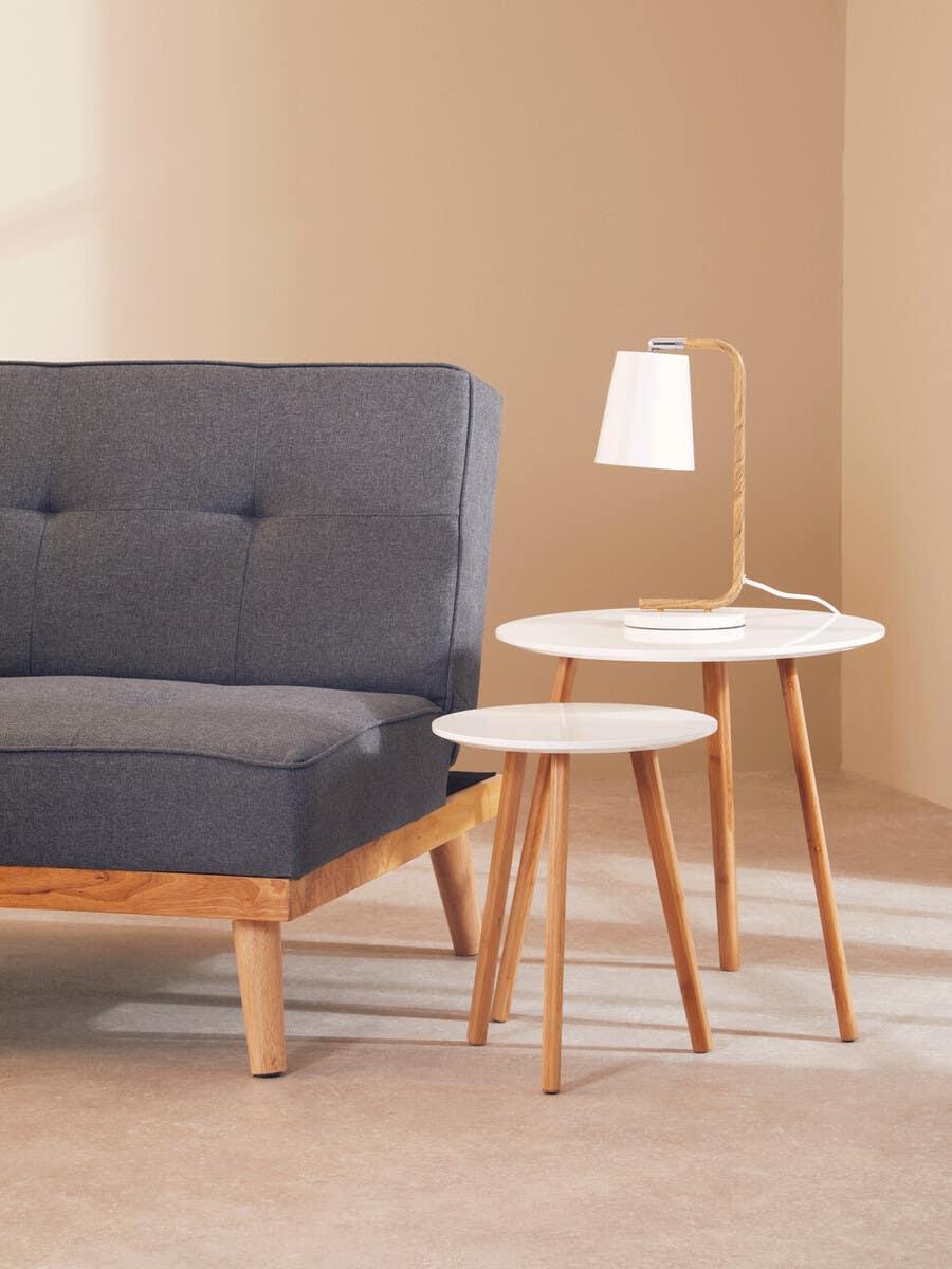 Grey fabric sofa with wooden legs beside two nesting tables with lamp in modern living room