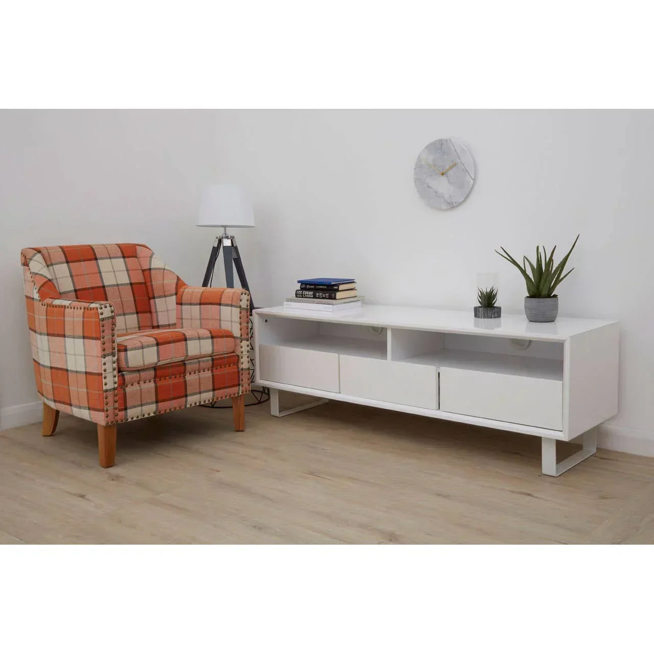Orange plaid armchair beside modern white TV unit with drawers, lamp, and potted plants