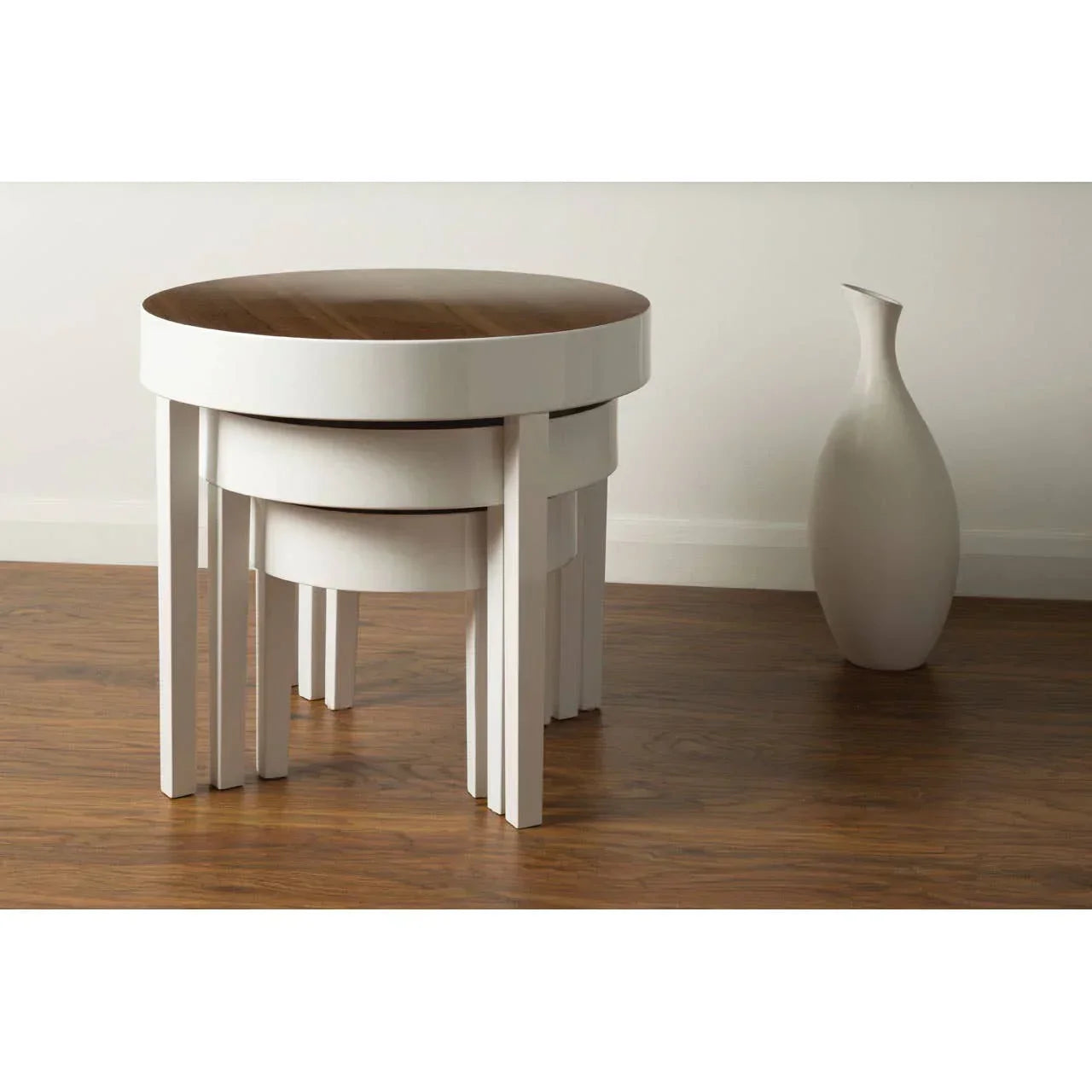 Round nesting tables with white legs and wood tops beside a modern ceramic vase on hardwood floor