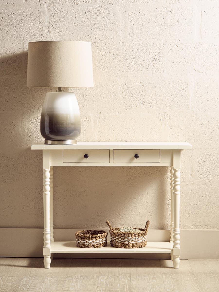 Cream console table with drawers, beige table lamp, and woven baskets on lower shelf