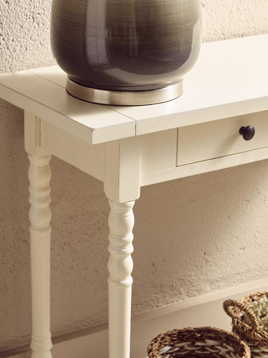 Cream console table with turned legs, drawer, and ceramic vase on top