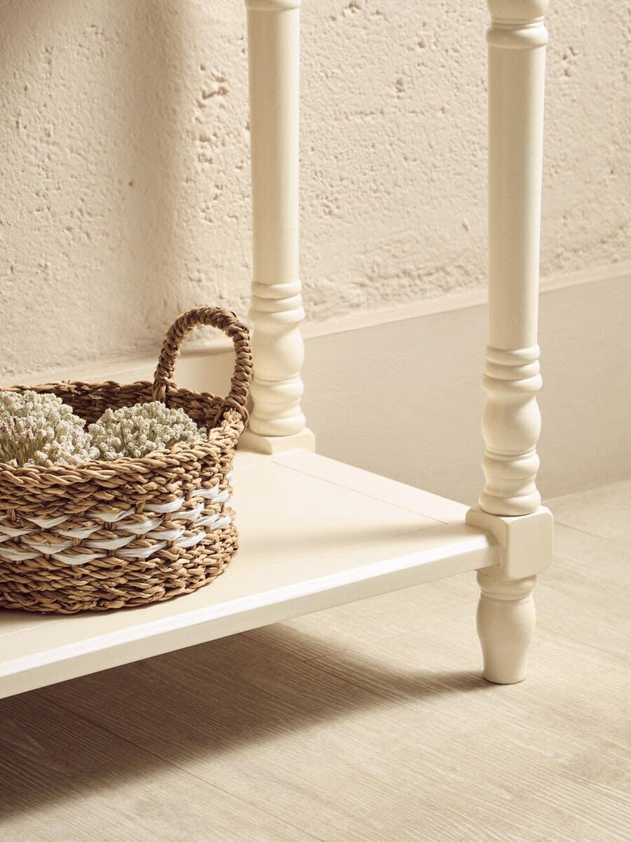 Cream painted wooden table leg and lower shelf with woven basket on light wood floor