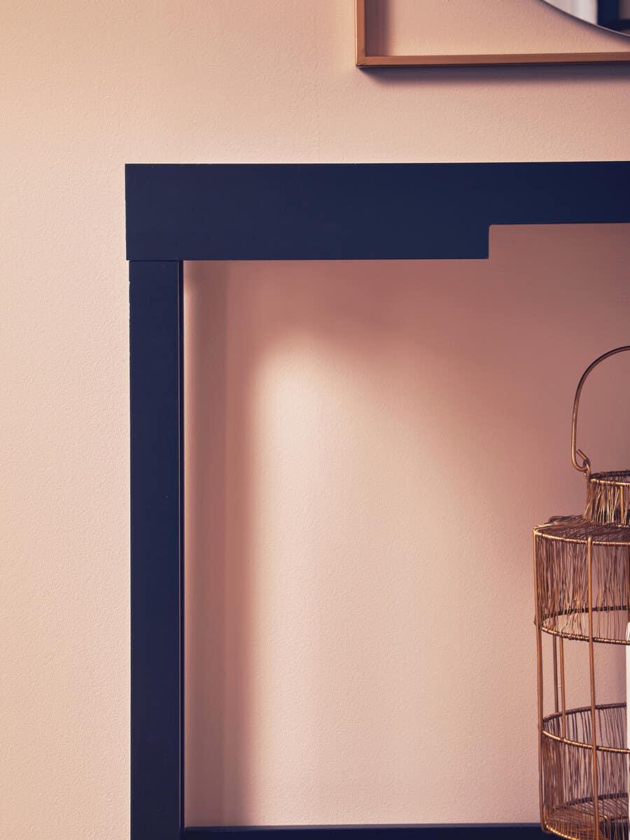 Black wooden console table with gold wire basket beside blush wall